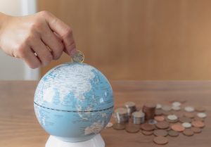 Business woman hand putting one pound coin in to piggy bank for donate money helping the earth,